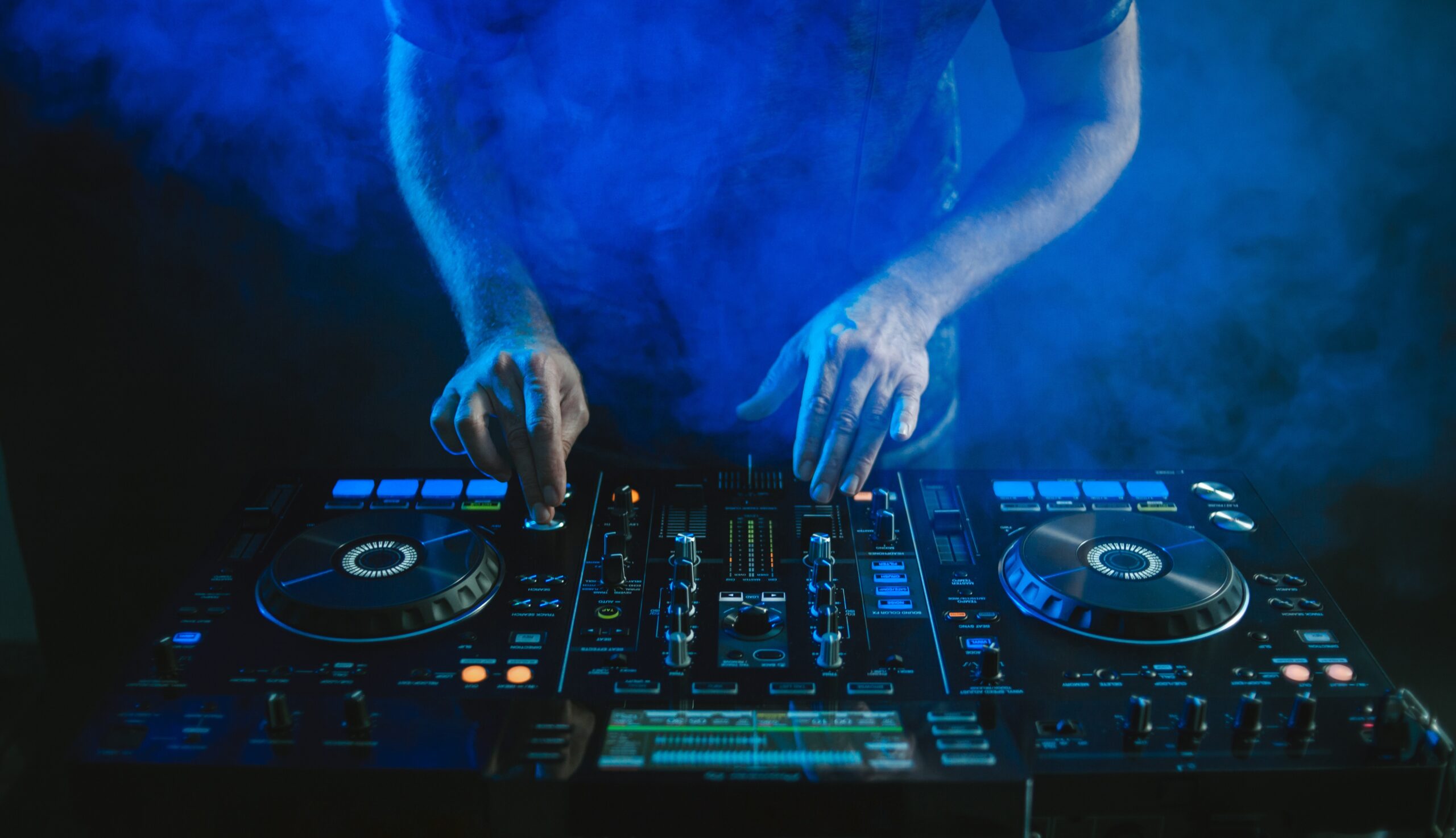 Closeup of a DJ working under the blue lights against a dark background in a studio